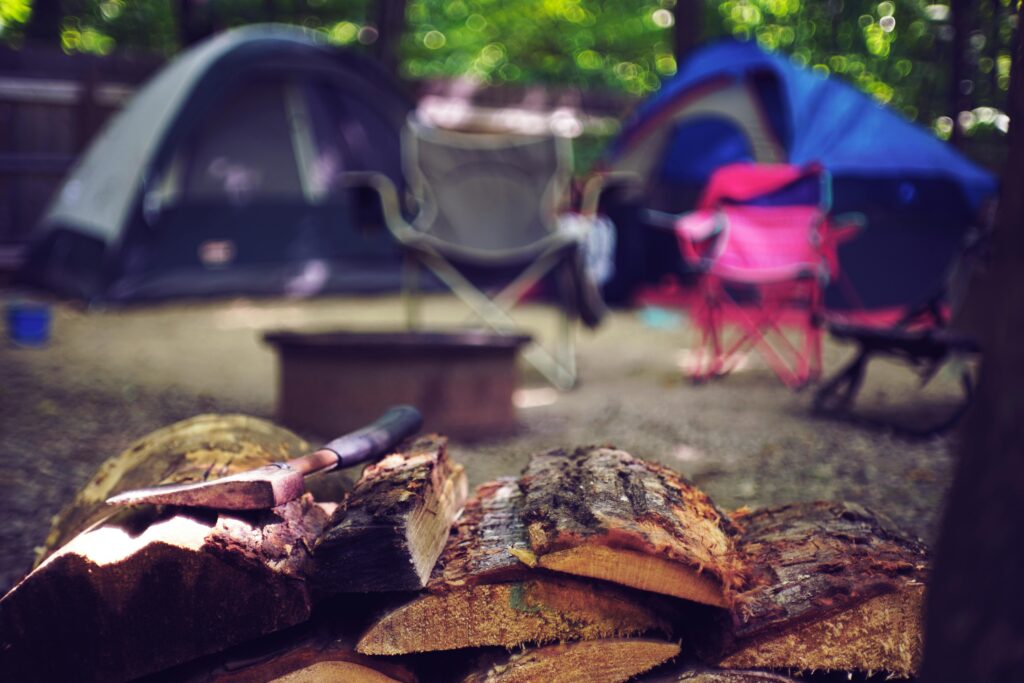 camping sleeping gear, A serene campsite featuring tents, chairs, and a pile of firewood for a perfect summer getaway.