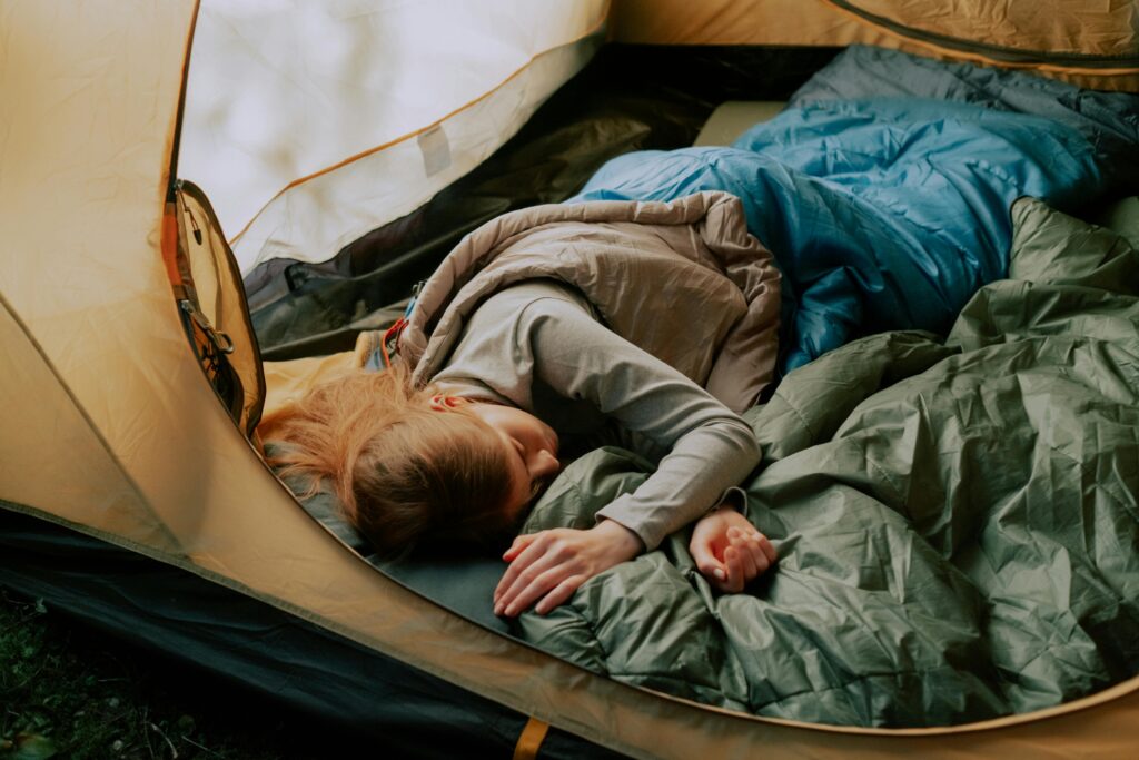 camping sleeping gear, A serene scene of a woman sleeping comfortably in a tent during a camping trip, surrounded by nature.