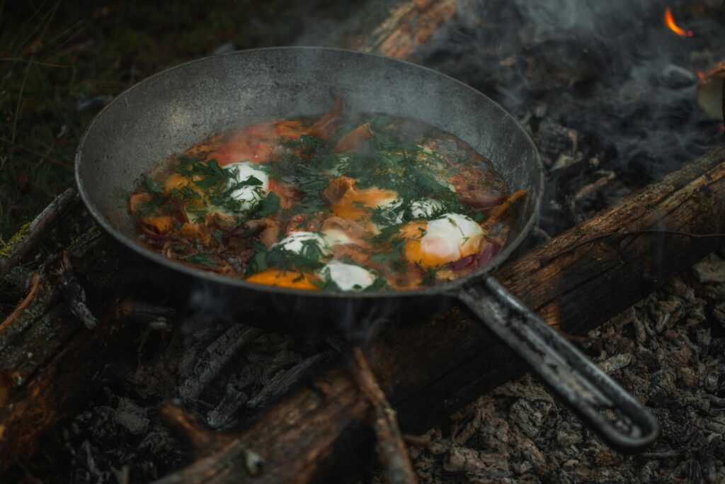 Delicious breakfast cooked over a campfire featuring eggs, herbs, and vegetables in a frying pan.