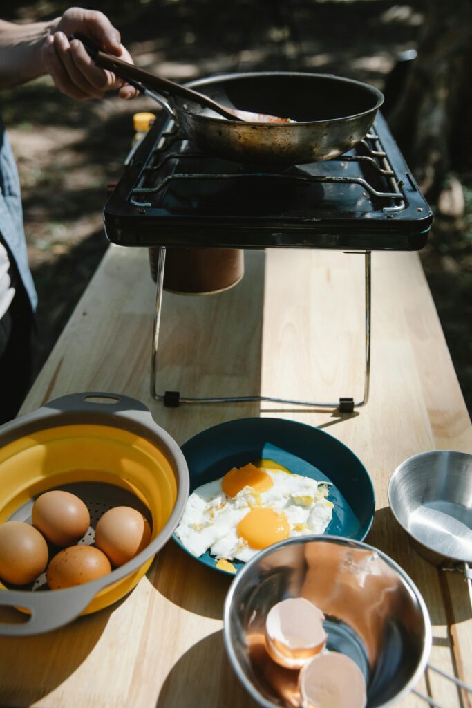 Crop unrecognizable male cooker frying eggs on skillet on metal stove in nature